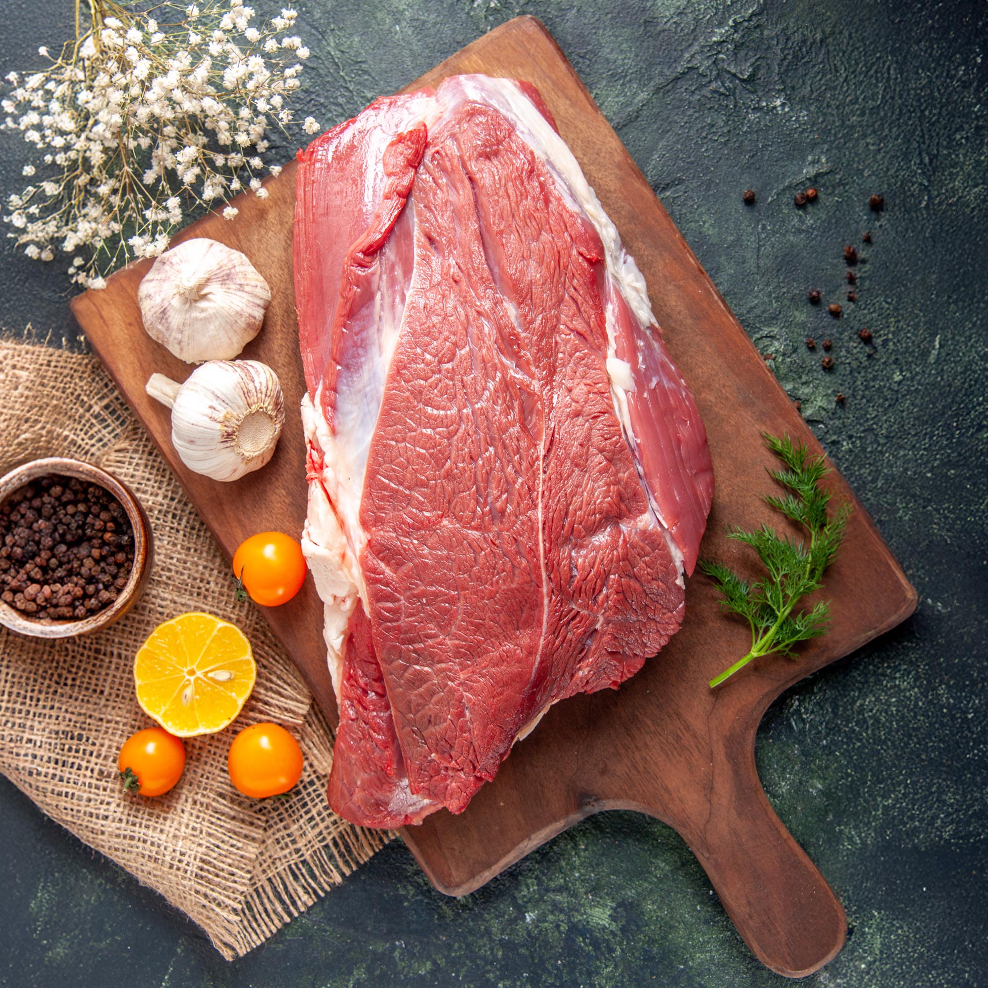 Premium Meat Supplier in the Middle East | Sidco Foods 1 vertical view fresh raw red meats green garlics brown wooden cutting board tomatoes pepper nude color towel knife dark color background copy